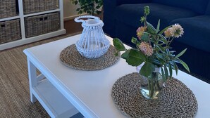 A living room with a white coffee table, wicker baskets, a blue sofa, a potted plant, and a TV mounted on the wall.