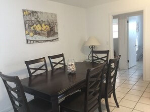 Un área de comedor con una mesa y sillas de madera oscura, un florero de vidrio con conchas marinas, una lámpara de pared y un cuadro de limones.