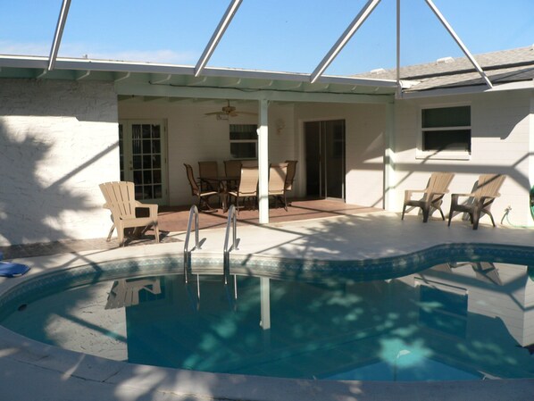 A swimming pool with a covered patio area, outdoor furniture, and a clear sky.