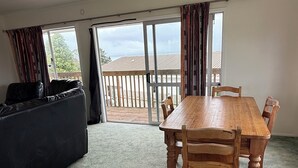 A room with a wooden dining table and chairs, a black sofa, and a view of a balcony with a wooden railing. - Tokerau Beach Paradise (Tokerau Beach)