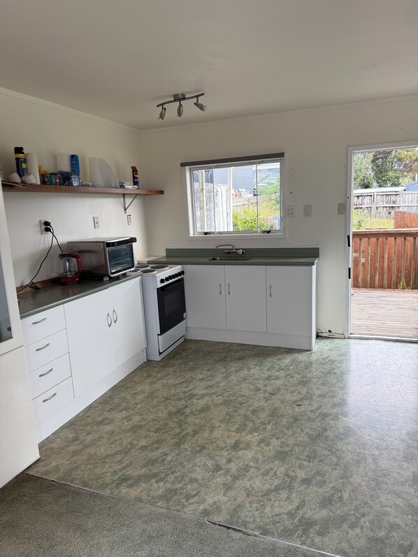 A compact kitchen with white cabinets, a built-in oven, a microwave, and a small countertop. There is a window above the sink, and a door leading to a backyard.