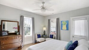 Une chambre à coucher comprenant un lit, deux chaises, une commode, un ventilateur de plafond et un tableau.