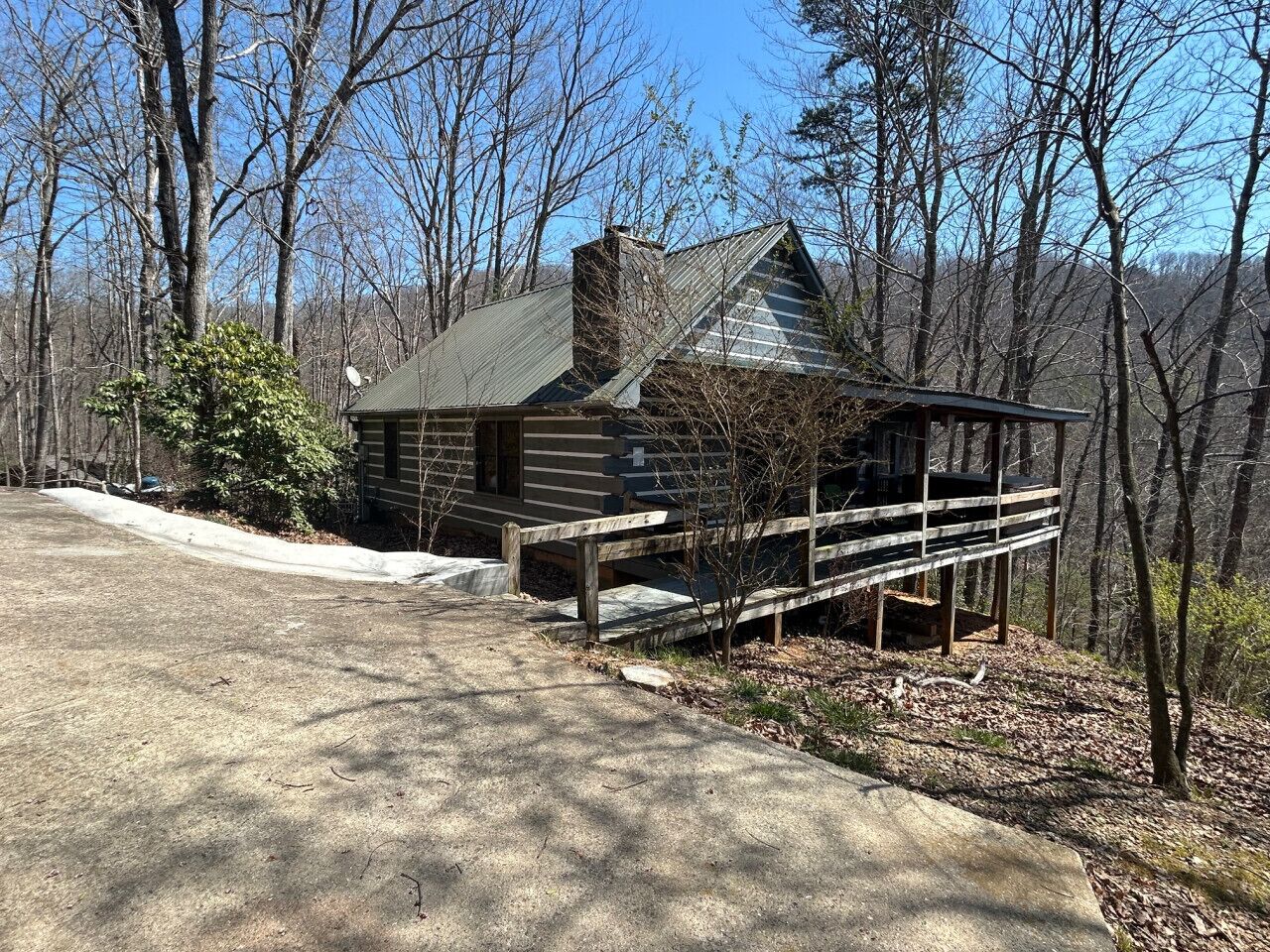 A cabin with a wooden deck and a chimney, surrounded by trees.