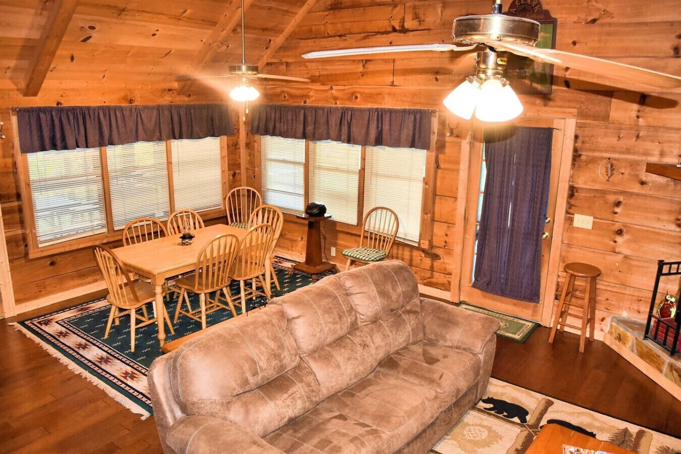 A cozy cabin interior with a dining table, chairs, a sofa, and a ceiling fan.