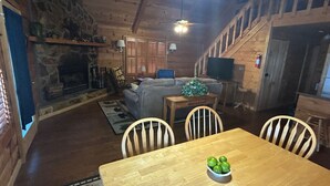 A cozy cabin interior with a dining table, chairs, a sofa, a fireplace, and a staircase. - Trail`s End-Hot tub-Wi-Fi,-pets ok-Pool Table-Fireplace-Screened Porch-Activities (Morganton)