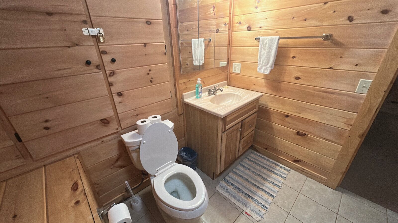 Ein Badezimmer im Holzblockhausstil mit Toilette, Waschbecken und Stauraumschränken.