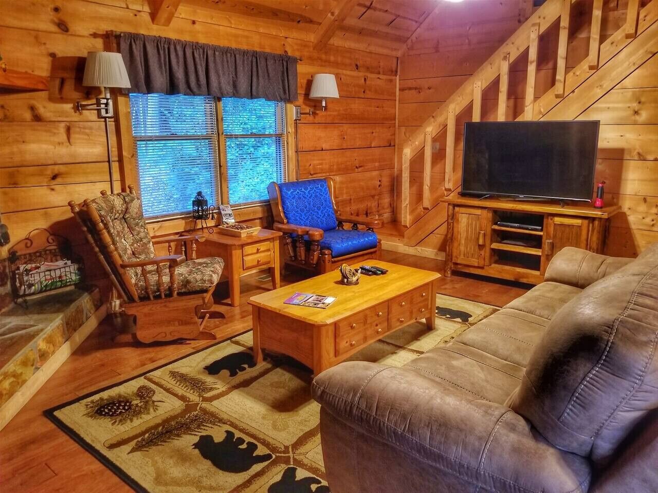 L'interno accogliente di una baita con arredamento in legno, un divano, una poltrona blu, un tavolino da caffè in legno e un televisore su un mobile.