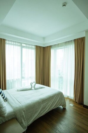 A hotel room with a large bed, two windows with curtains, and a city view. - Luxury Condo 904 at The Padgett Place (Cebu City)
