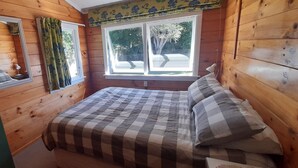 A wooden-paneled room with a bed, a window with curtains, and a mirror. - Quaint Lockwood River Cottage (Turangi)