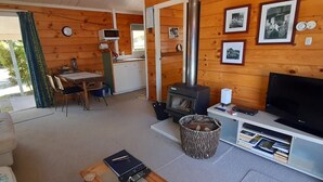 A cozy cabin with a wooden interior, a dining area, a TV, and a fireplace. - Quaint Lockwood River Cottage (Turangi)