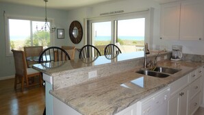 A kitchen with granite countertops, a sink, and a dining area with wicker chairs. - Beachfront - Romantic - Relaxing - Panoramic Views - Little Gasparilla Island  (Placida)