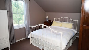 Un dormitorio con estructura de cama metálica blanca, una mesita de noche con lámpara y una ventana con cortinas.