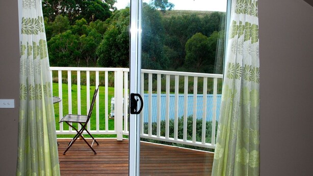 Una terraza de madera con barandilla blanca, una silla y una puerta con manija.