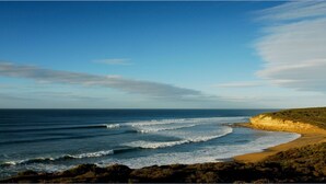 Un paisaje costero con playa, olas del océano y terreno rocoso.