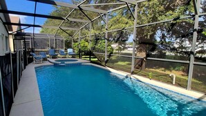 An indoor swimming pool with a sunshade structure, lounge chairs, and a view of the surrounding greenery.