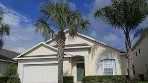A single-story house with a garage, palm trees, and a well-maintained lawn.
