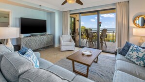 Ein Wohnzimmer mit Flachbildfernseher, einer Sofagarnitur, einem Couchtisch und einem Balkon mit Sitzgelegenheit.