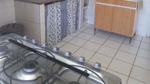 Una cucina con pareti rivestite di piastrelle bianche, un fornello a gas, un lavello con rubinetto e un forno a microonde su un mobiletto in legno.