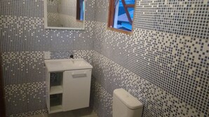 Et badeværelse med en hvid vask, et spejl og et toilet. Væggene er beklædt med små, firkantede mosaikfliser.