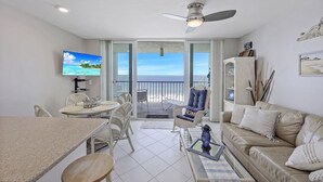 Ein Wohnzimmer mit Fernseher, Esstisch, Stühlen, einer Couch und einem Balkon mit Meerblick.
