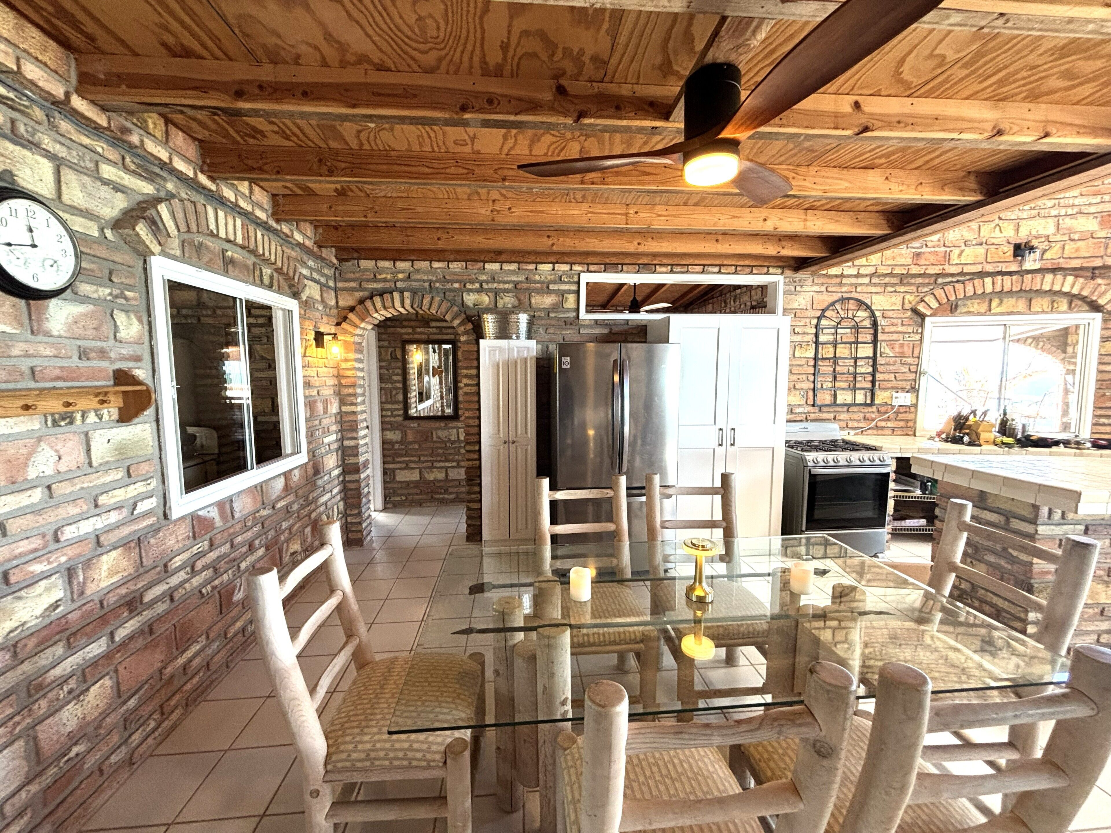 Une cuisine rustique avec un mur en briques, un plafond en bois et une table à manger en verre.