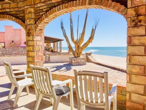 Un patio con sillas blancas y un árbol, con vista a la playa.