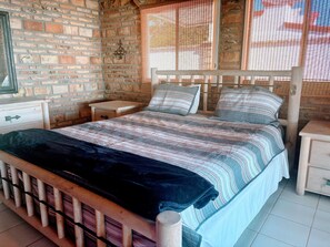 A room with a brick wall, a bed with striped bedding, a wooden headboard, a nightstand, and a small table. - Promo - Awesome  -Beach Front Villa on Sandy Beach  - Hi Speed Wi-Fi (San Felipe)