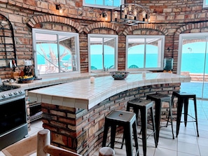 Una cocina con pared de ladrillo, ventanas amplias y vista al mar.