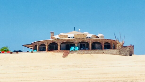 Un edificio grande de varios pisos con techo plano y múltiples arcos, ubicado en una pendiente arenosa.