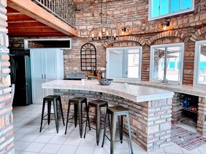 A kitchen with a brick wall, a large island with stools, and a view through the windows. - Promo - Awesome -Beach Front Villa on Sandy Beach - Hi Speed Wi-Fi (San Felipe)