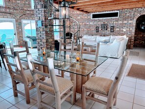 A dining area with a glass table surrounded by wooden chairs, a brick wall, and a view of the sea. - Promo - Awesome  -Beach Front Villa on Sandy Beach  - Hi Speed Wi-Fi (San Felipe)