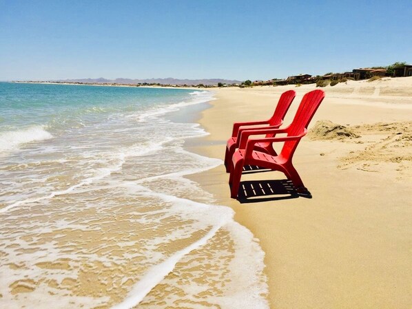 Una playa con dos sillas rojas mirando al océano.