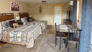 Una habitación con dos camas, una mesita, una silla, un televisor y una puerta.