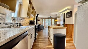 Uma cozinha com bancada de mármore, lava-louças, fogão e lixeira preta.