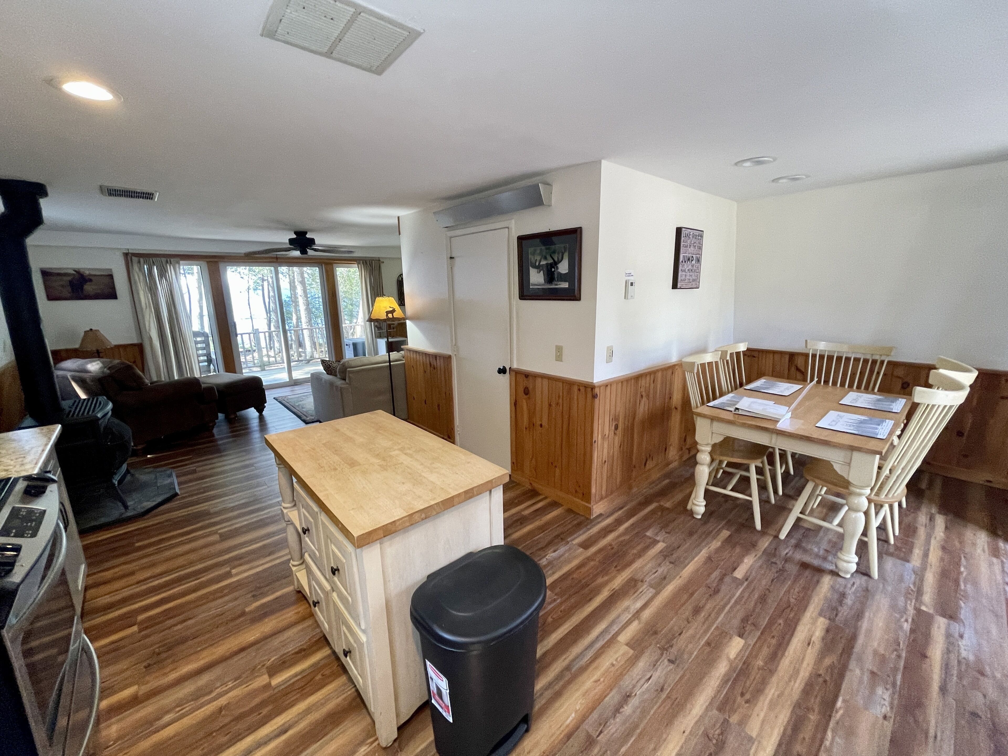 A spacious living area with a wooden floor, a dining table with chairs, a sofa, and a kitchen area with a stove.