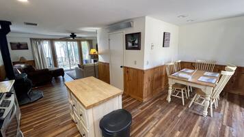 A spacious living area with a wooden floor, a dining table with chairs, a sofa, and a kitchen area with a stove.