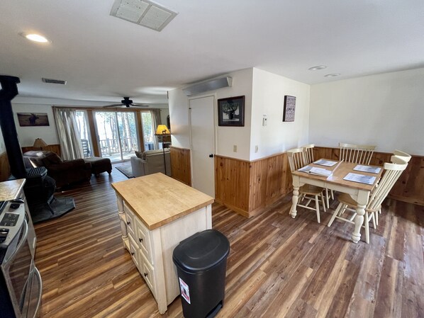 Un amplio salón con suelo de madera, una mesa de comedor con sillas, un sofá y una zona de cocina con estufa.