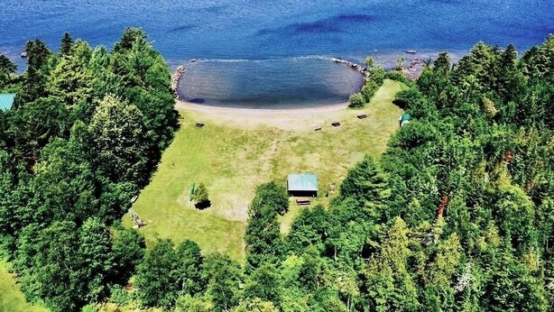 Uma propriedade à beira do lago com uma cabana pequena, rodeada por uma floresta densa e uma vista desimpedida do lago.