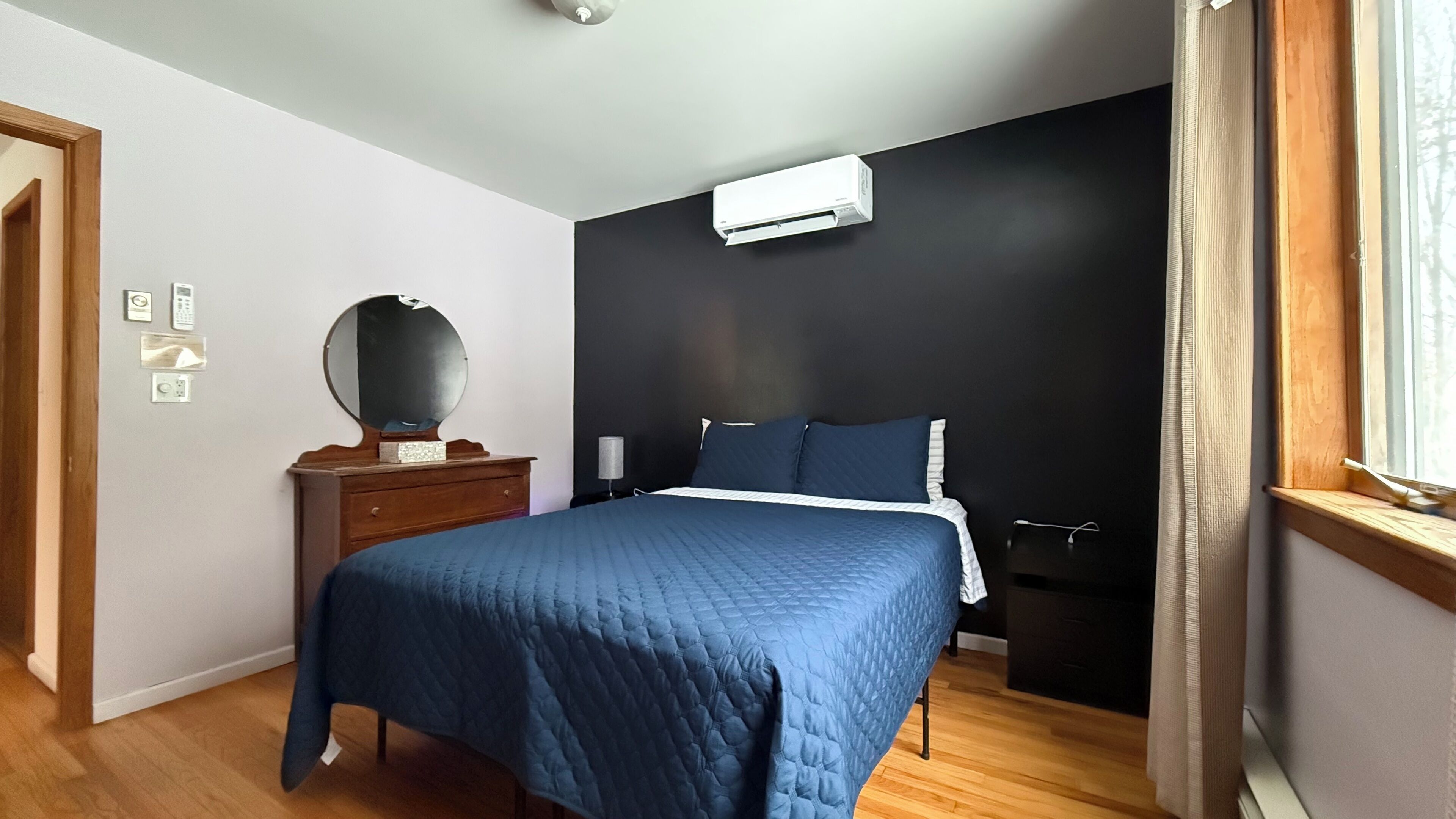 A bedroom with a bed, a dresser, a mirror, and an air conditioning unit.