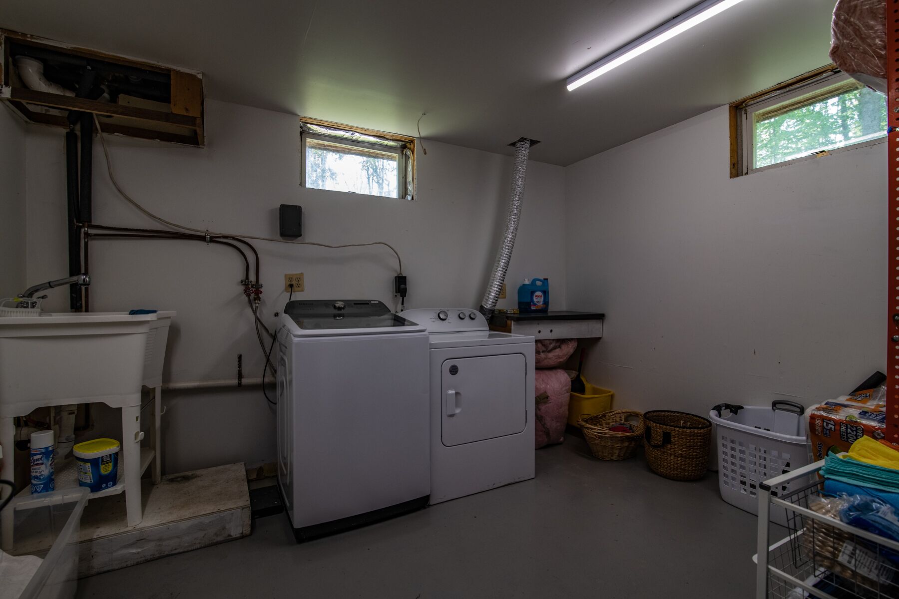 Ein Waschraum mit Waschmaschine, Trockner und Waschbecken. Es gibt Fenster, einen Deckenlüfter und Wäschekörbe.