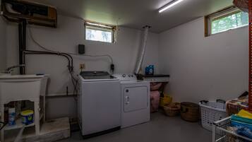 Ein Waschraum mit Waschmaschine, Trockner und Waschbecken. Es gibt Fenster, einen Deckenlüfter und Wäschekörbe.
