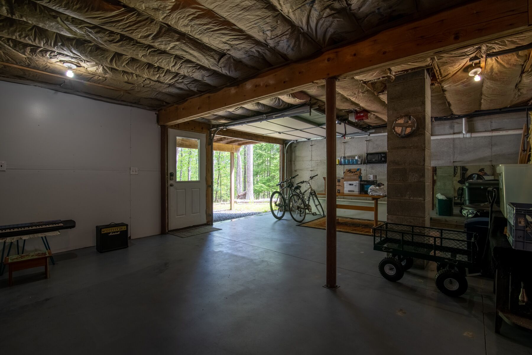 Un grand garage doté d’un sol en béton, de poutres en bois et d’un vélo.