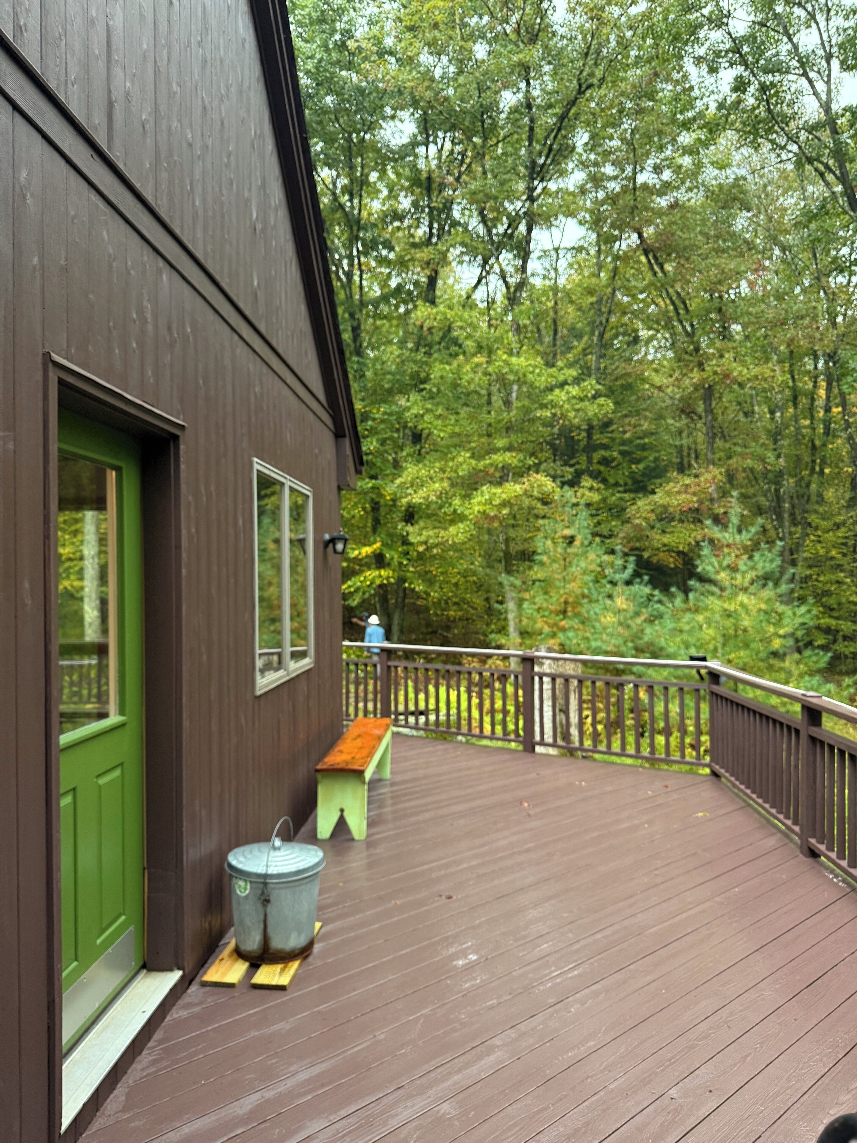 A wooden deck with a green door and windows, a bench, and a trash can.
