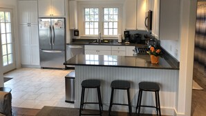 Una cocina moderna con armarios blancos, un refrigerador de acero inoxidable, una isla grande con taburetes de bar y un ventanal que proporciona luz natural.