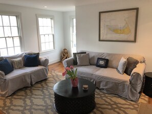 A living room with striped sofas, a round coffee table with a vase, and a framed map on the wall. - Renovated Home For Family or Large Group! (Nantucket)