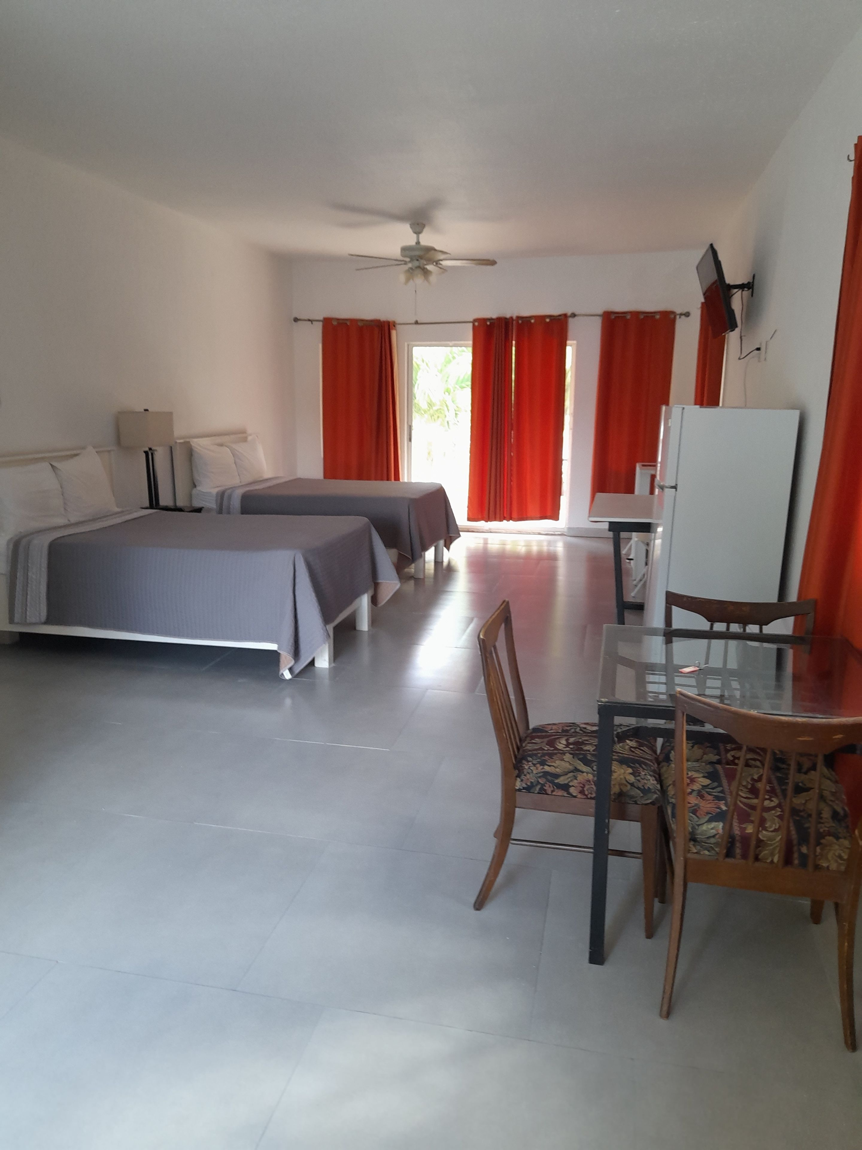 Habitación de hotel con dos camas, una mesa de comedor con sillas, ventilador de techo y refrigerador.