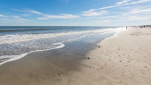 A wide sandy beach with gentle waves, a clear sky, and a few people in the distance. - Seacoast 7- Top Floor Villa - Unobstructed Ocean Views - Elevator (Folly Beach)