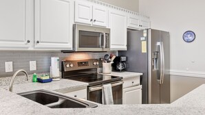 A modern kitchen with white cabinets, stainless steel appliances, granite countertops, and a built-in microwave. - Seacoast 7- Top Floor Villa - Unobstructed Ocean Views - Elevator (Folly Beach)