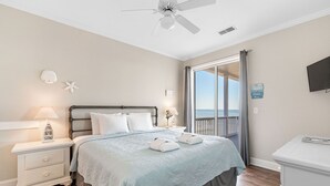 A bedroom with a bed, nightstand, lamp, and a view of the ocean through a balcony. - Seacoast 7- Top Floor Villa - Unobstructed Ocean Views - Elevator (Folly Beach)