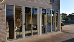 Un bâtiment doté de grandes portes coulissantes en verre qui donnent sur un espace extérieur aménagé avec des chaises et des tables.
